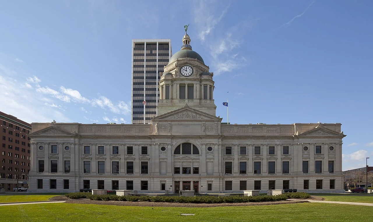 Allen County Courthouse’s stone facade and clock tower across a green lawn.
