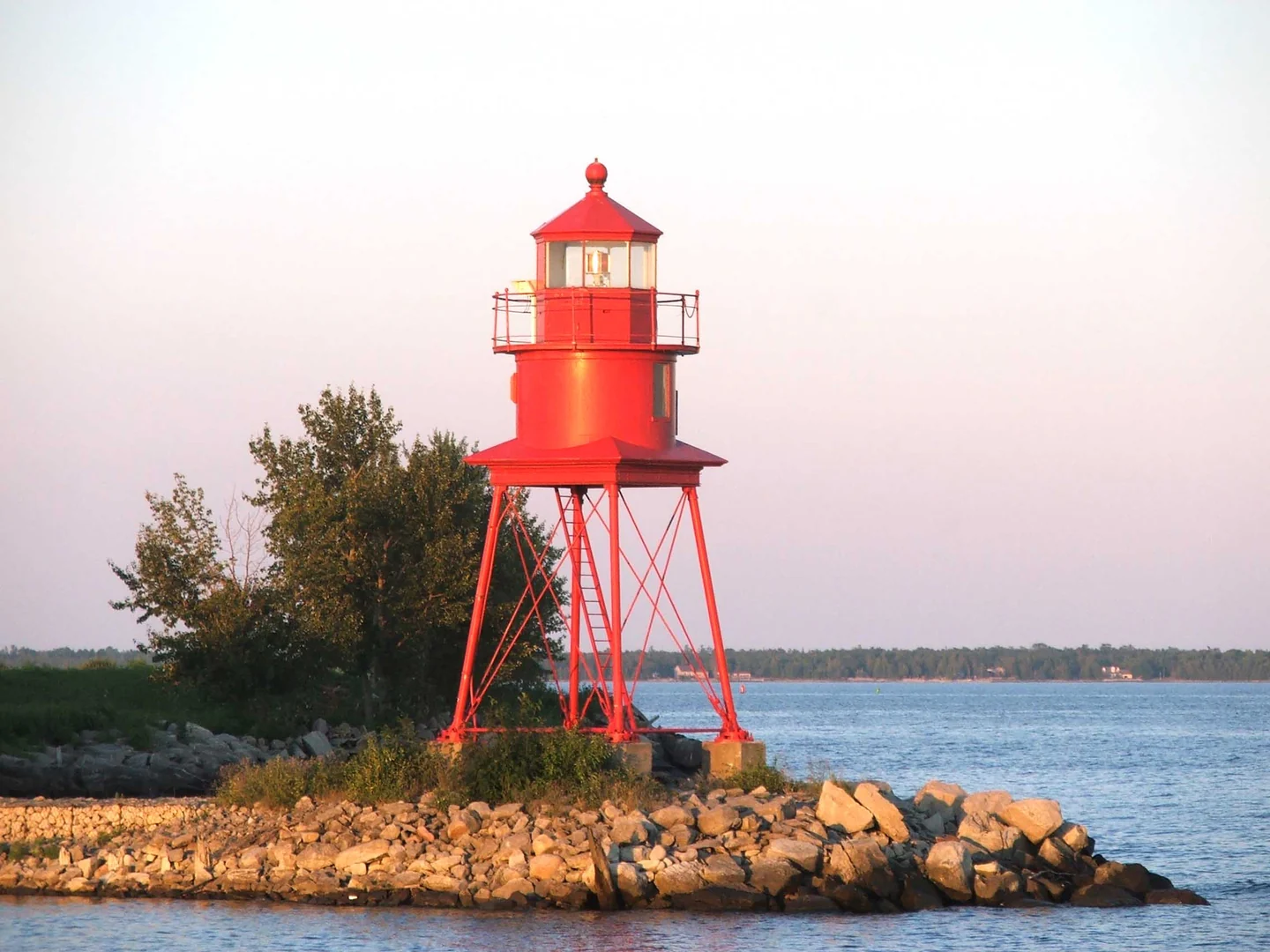 The red Alpena Light on a rocky point beside the water in Alpena.